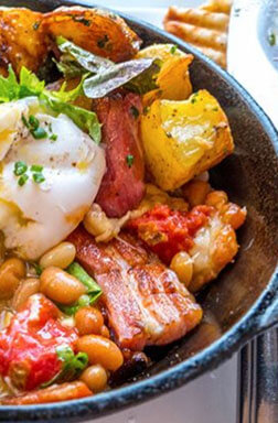 Cast-iron skillet with beans, bacon, potatoes and a poached egg